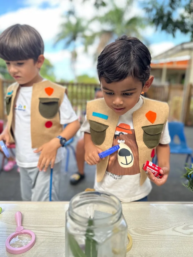 Dos niños observan una hoja dentro de un frasco de vidrio al aire libre